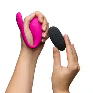 Hands holding pink wearable massager and remote control.